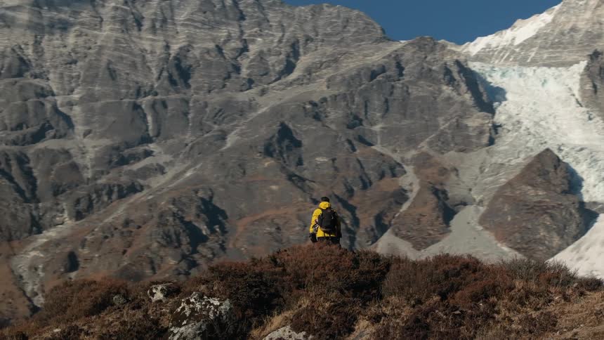 A hiker stands on a mountain ridge gazing at snowcapped peaks in the distance