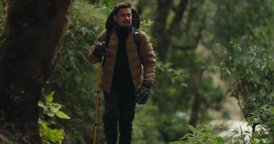 Man in brown puffy jacket hiking up a steep dirt trail in the wilderness