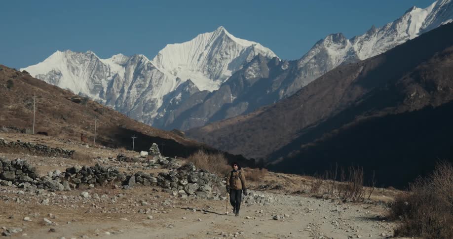Man walking along a dirt road surrounded by mountains in winter