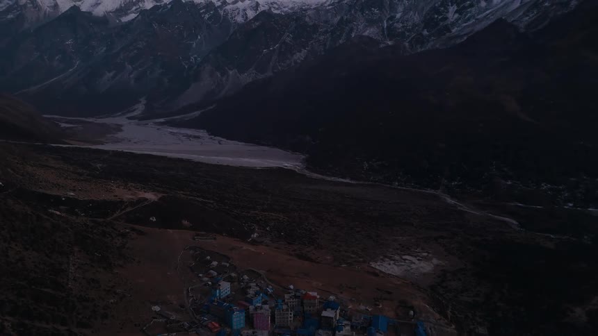 Aerial panorama of a village on a plateau surrounded by snowy mountains on a purple morning