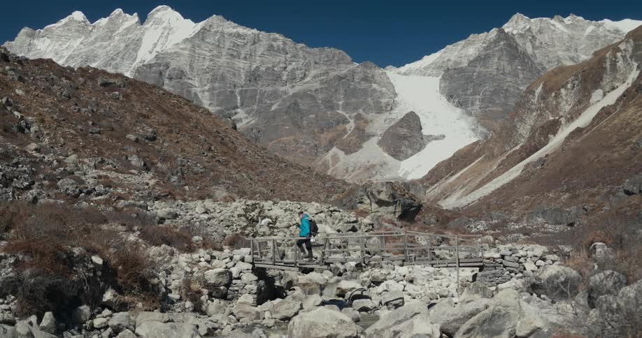 A hiker on a rocky valley crosses over a primitive wooden bridge