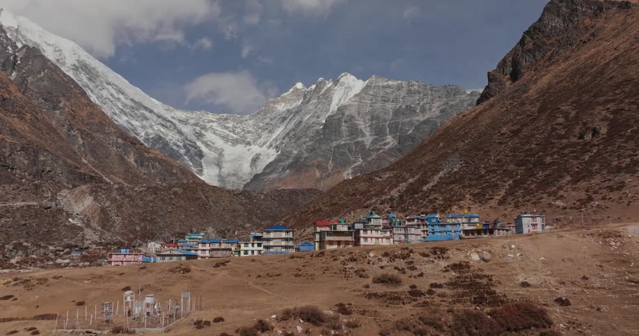 A village with some blueroofed houses in the middle of mountains with a snowcovered peak