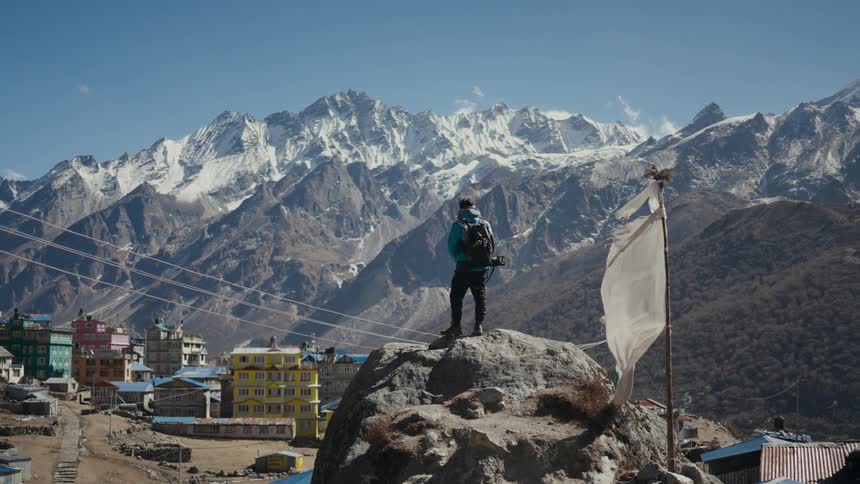 Panorama of a man on a rock peak in front of a village and surrounded by snowy mountains in winter