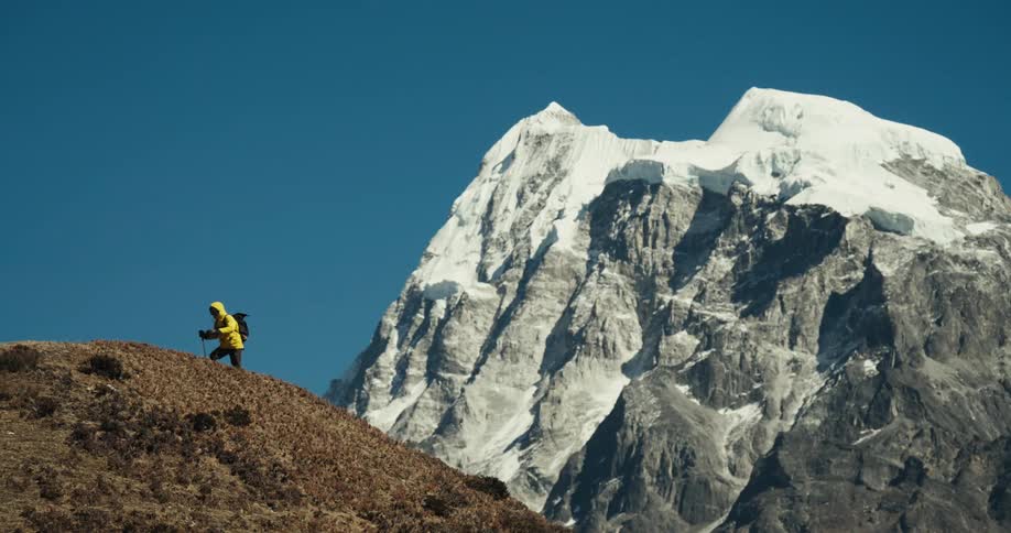 Man climbing a cliff with a natural view of mountains around with snow on a blue sky day