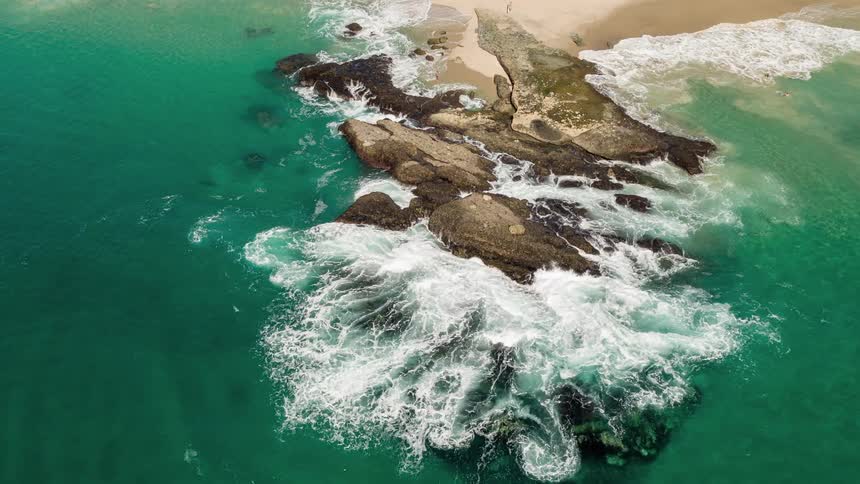 An aerial view of a rocky coastline with large waves crashing against the rocks