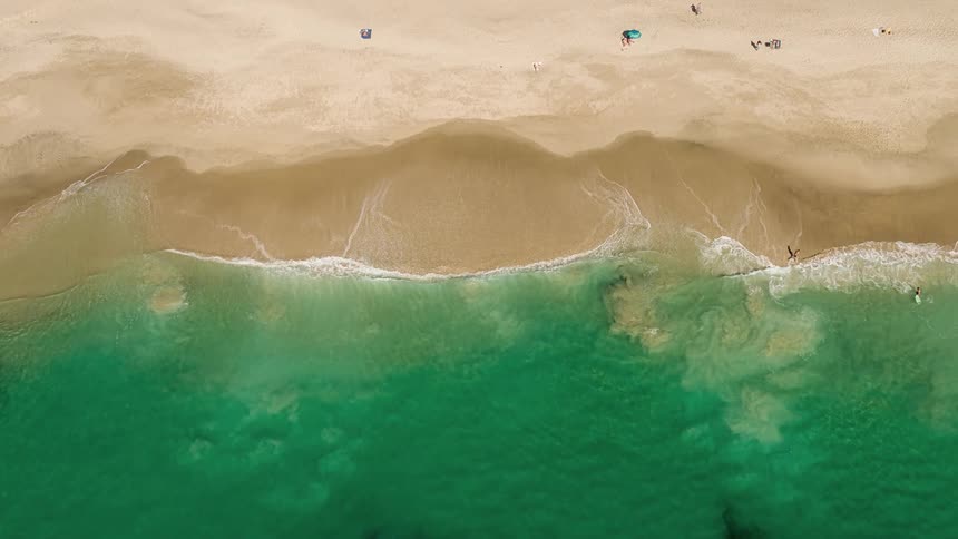 Aerial of waves crashing on a sandy shoreline