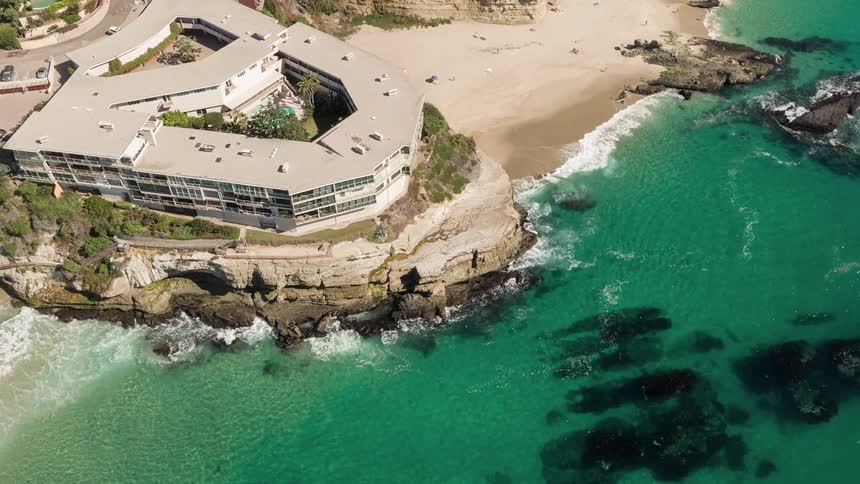A resort in front of a sandy beach and crystal clear water with many rocks in the water