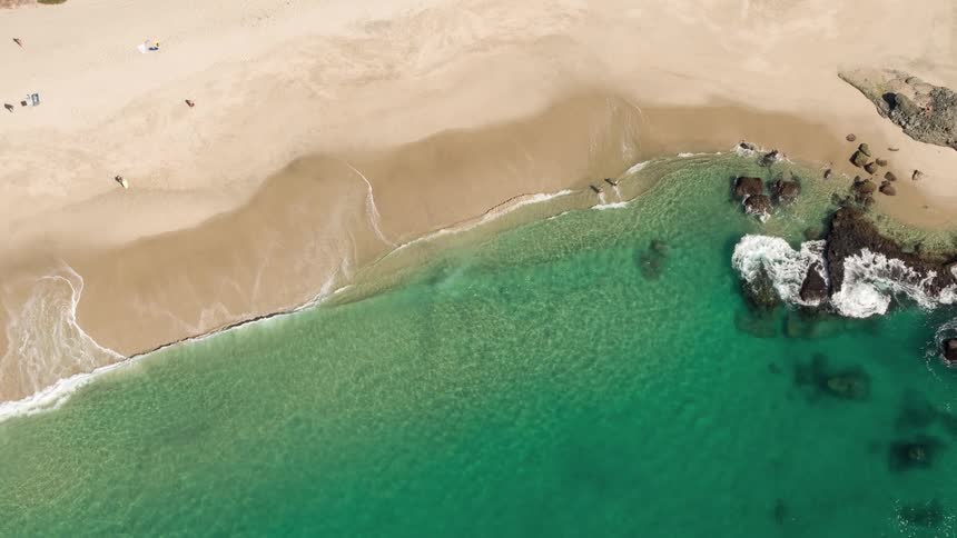 An aerial view of a beach with crystal clear water and small waves hitting the shore