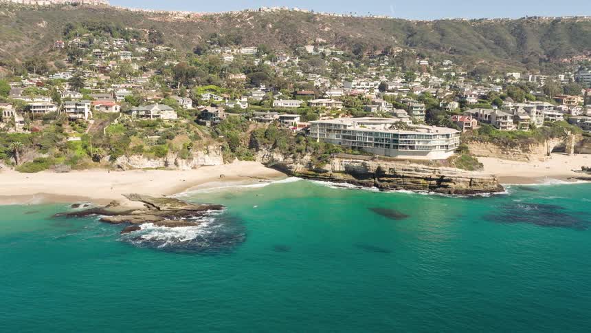 A resort on top of rocks in front of a beach with crystal clear water is behind a town