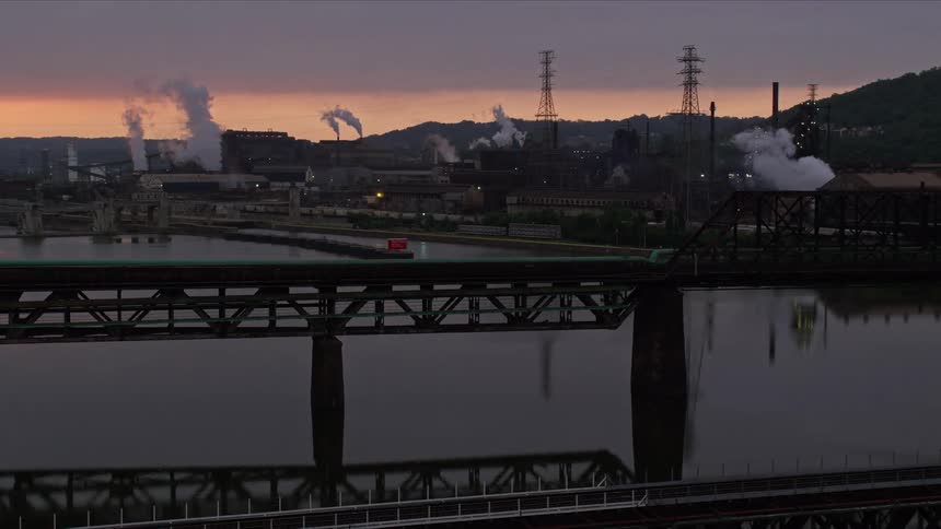 Panorama of factories with smoke chimneys next to a water deposit on a purple sky day with the silhouette of mountains on the horizon