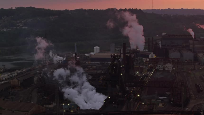 An aerial view of a factory with many chimneys throwing smoke upwards