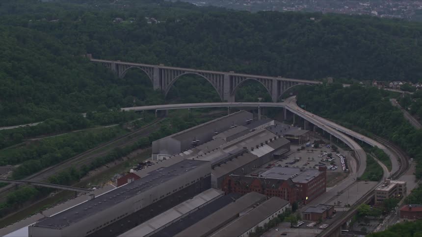 Aerial panorama of factory warehouses on the edge of the highway and hills with forests