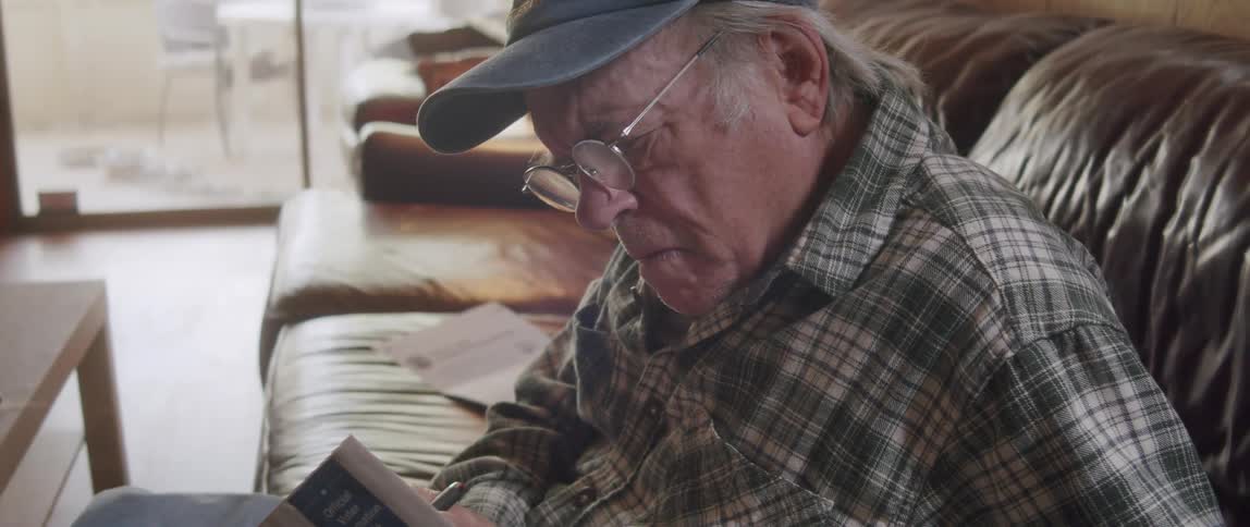 An old man sitting on a leather couch makes notes on a magazine about elections