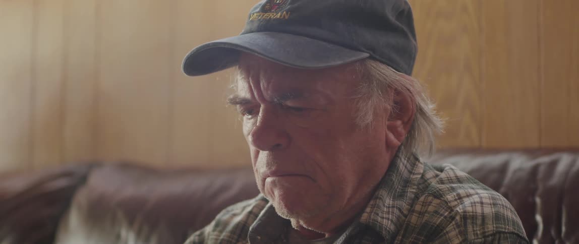 Elderly man sitting reading taking off his glasses and looking and shaking his head with a sign of denial