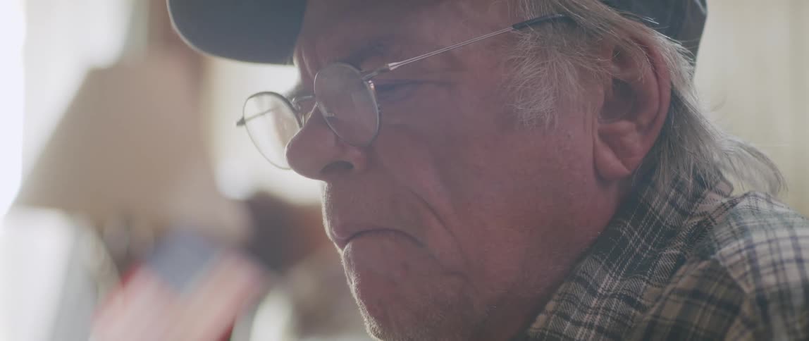 An elderly man is sitting while reading something and then takes off his reading glasses