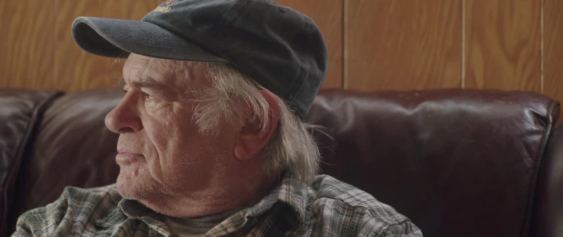 An elderly man reading the newspaper on the couch at home