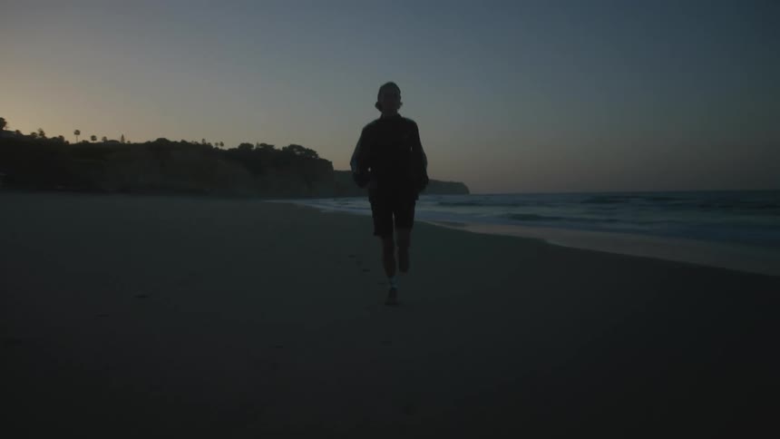 Silhouette of a person running near the shore line on the beach at dawn