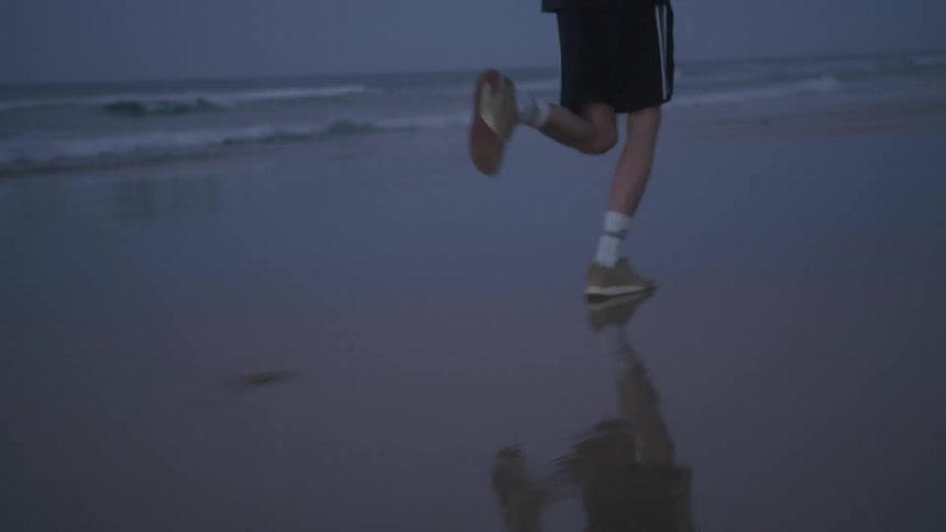 Man in shorts running along a beach by the shoreline at twilight