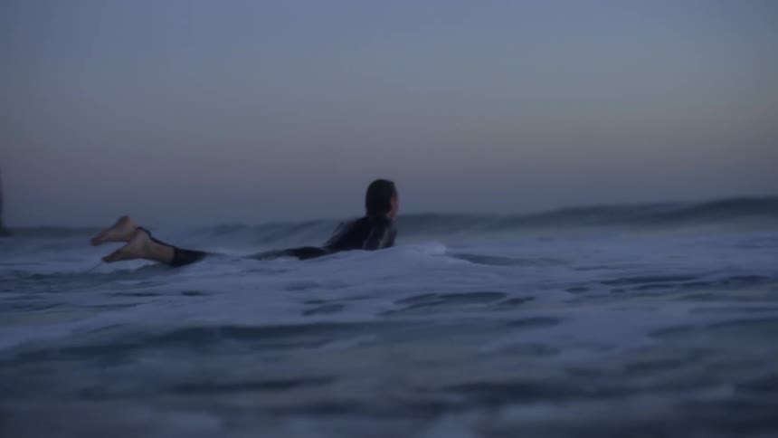 Surfer paddling in the ocean at dawn towards a wave