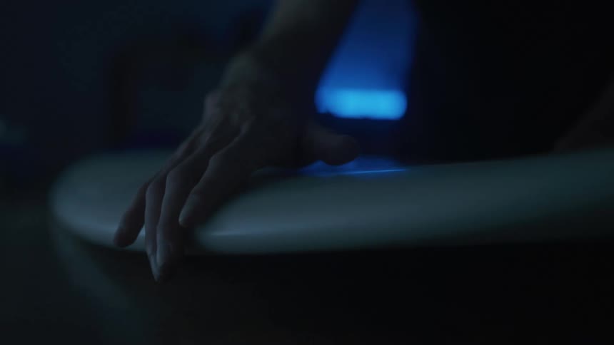 A man is holding a surfboard in the dark room