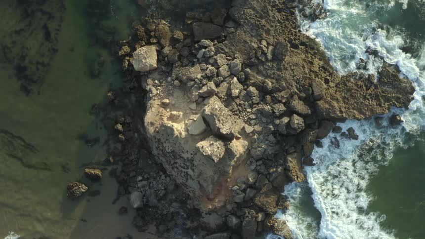 Waves crash against a pile of rocks on a coast