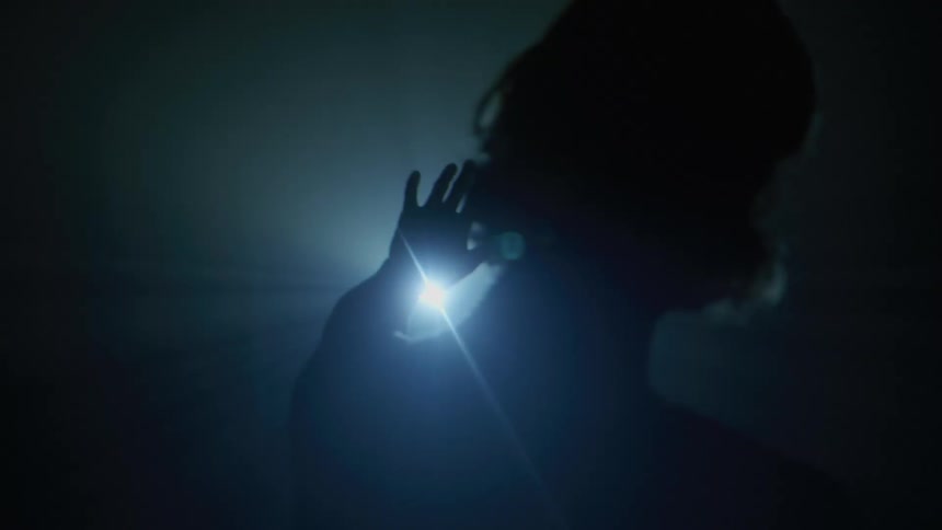 A person in the dark with a bright light shining towards them trying to cover it with their hand
