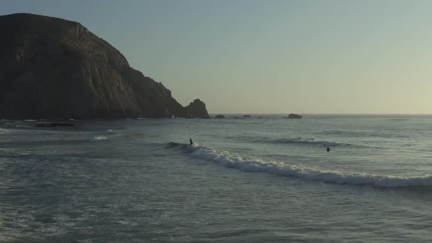 Surfers riding small waves on a beach at dusk