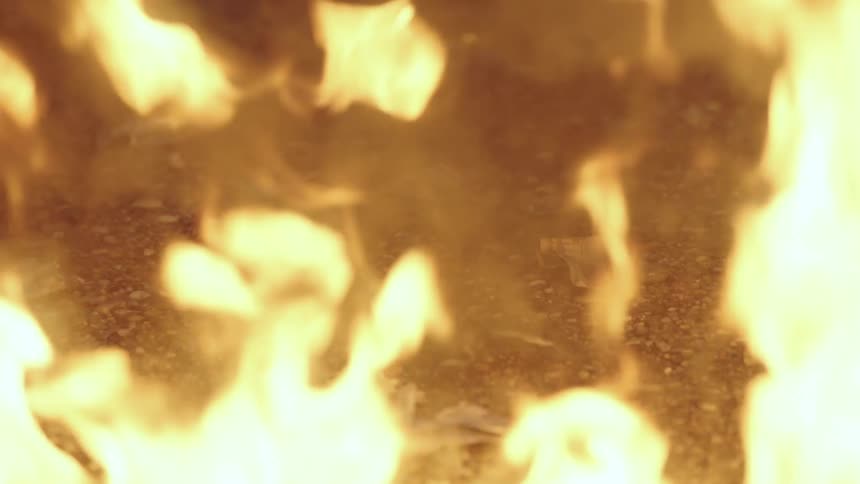 Flames flicker as a fire burn and release smoke while outdoors at nighttime