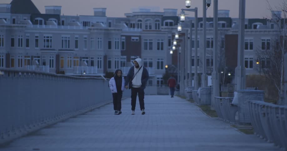 Father and daughter along with other pedestrians walk along walkway leading from apartment building