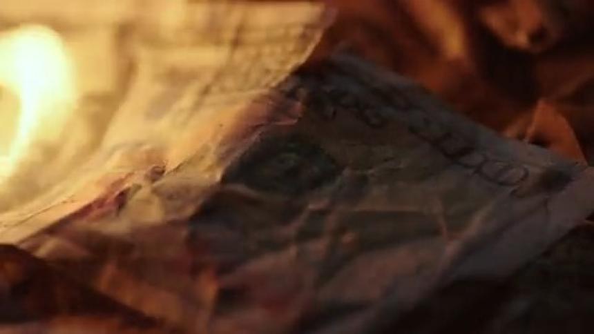 A one hundred dollar bill is slowly consumed by a burning flame