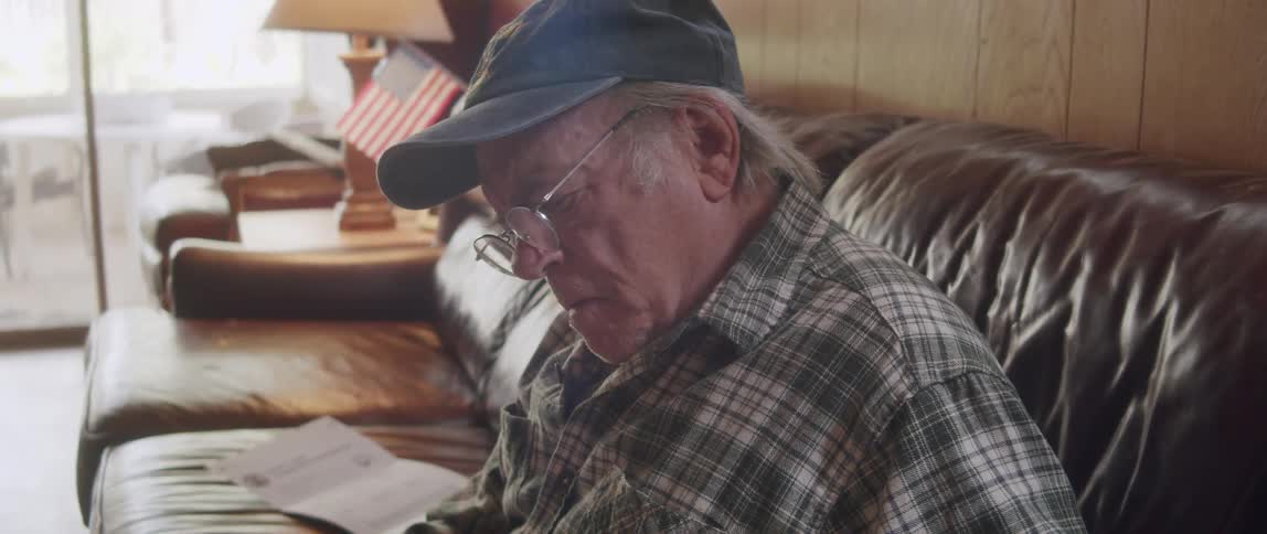 Man sitting on his living room couch reading a magazine as he sits up and writes in it with a pen