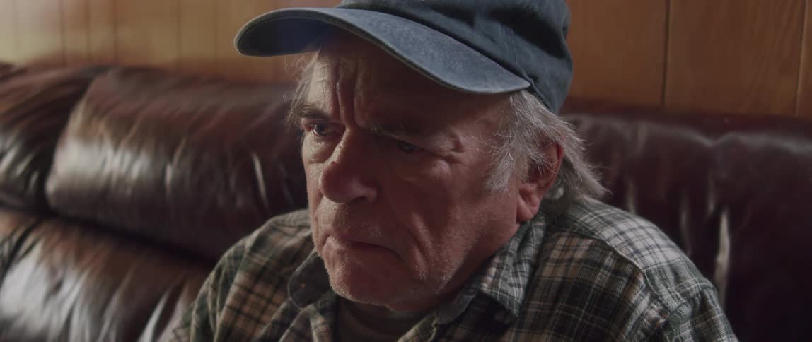 Man sitting on his living room couch reading a magazine as he stops to take off his glasses and think then puts them back on and continues reading