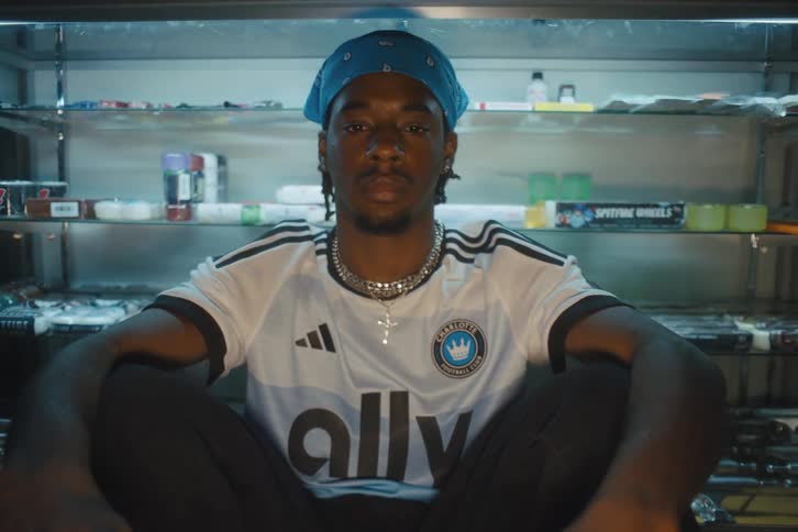 Man with a bandana on his head sitting posing in a soccer club tshirt