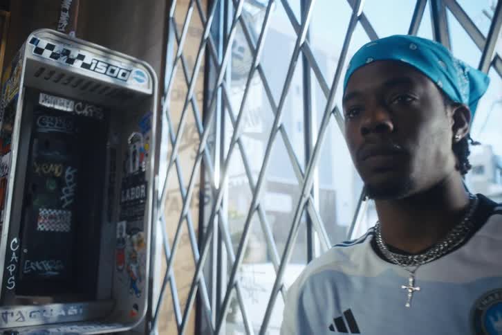 Man leans against barrier near graffiti covered empty public phone cupboard in city
