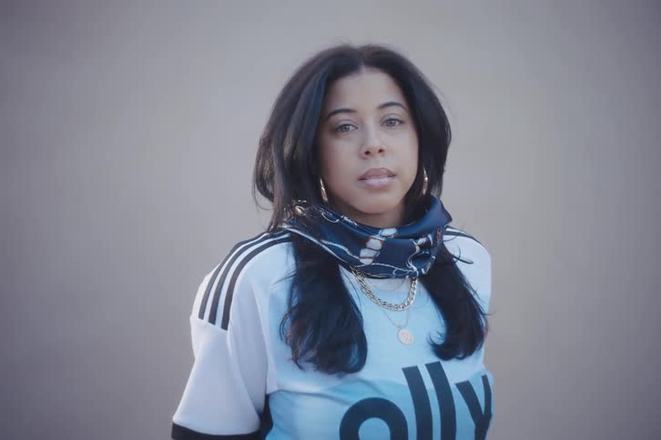 A woman is standing with a shirt with writing on it and she is looking forward and then looks to her left