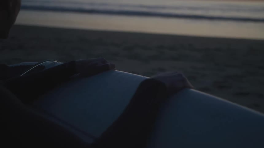 Surfer on beach holds surfboard while looking at red horizon
