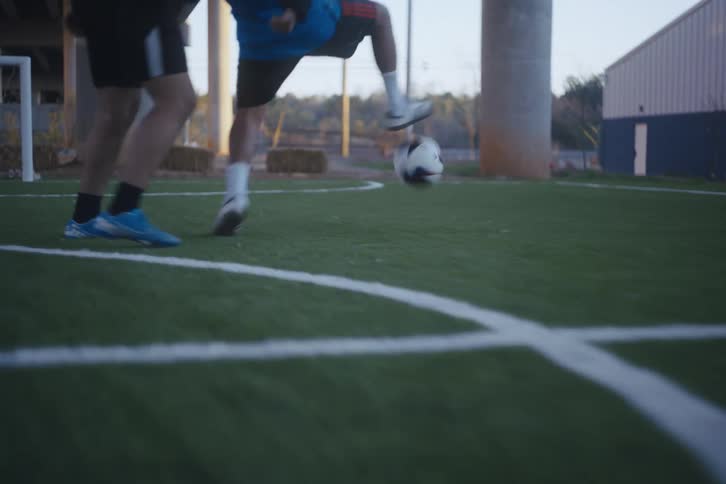 Legs of a man dribbling a soccer ball on a synthetic field and scoring the goal on a court below an overpass