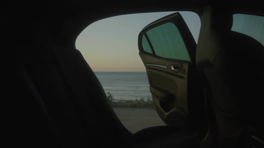 A beach at dusk seen from the interior of a parked vehicle