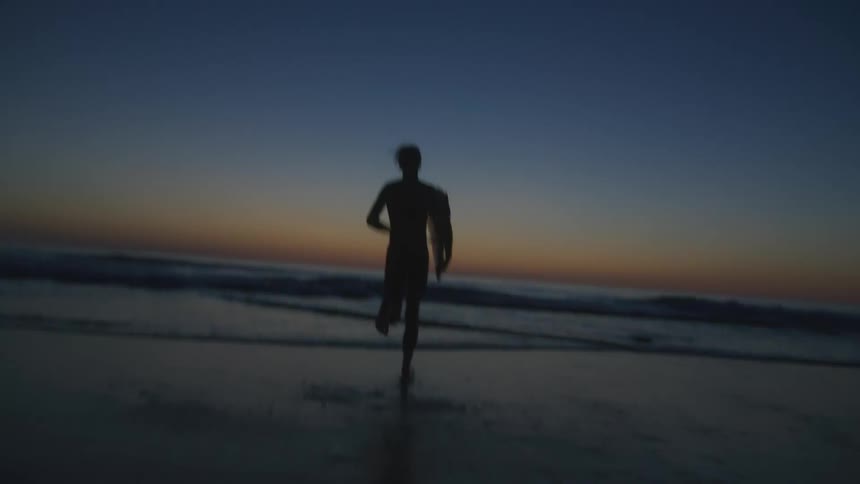 Silhouette of a person with his back running towards the sea with his surfboard in an orange morning sky