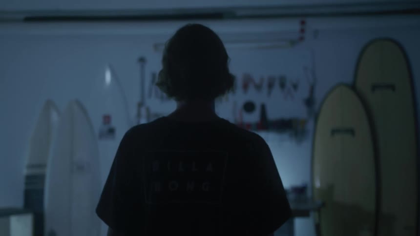 Silhouette of a person walking towards a wall with surfboards