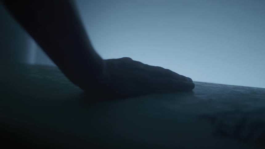 A mans hand gently caressing a surfboard in a dark room