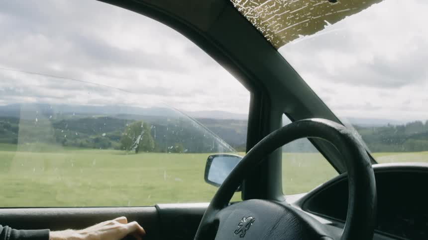 Hands of a man driving a vehicle and opening the window overlooking fields and mountains during the day