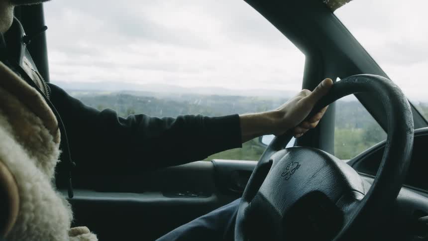 A man drives a car along a grass field on a rainy day