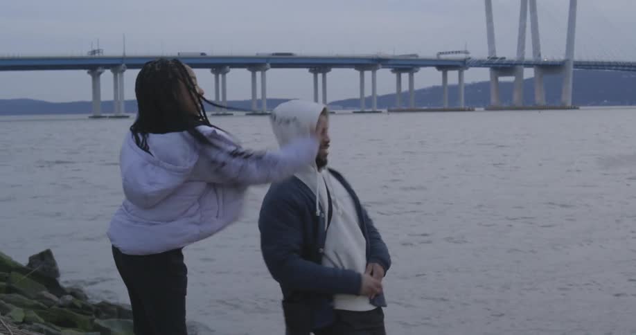 A man shows a woman how to skip a stone in a river