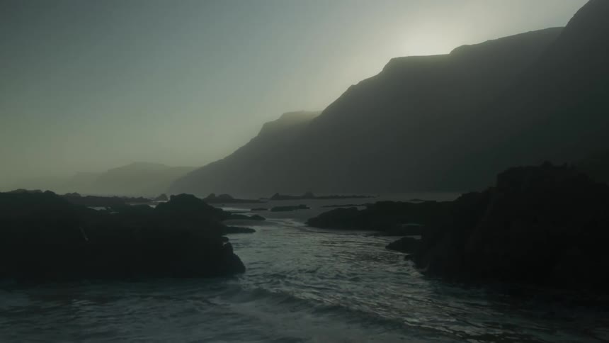 Shoreline of a dark beach next to mountains at dusk