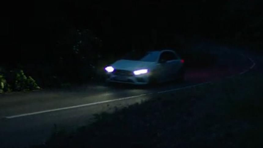 White sedan car passing a curve on the road at night with its headlights on