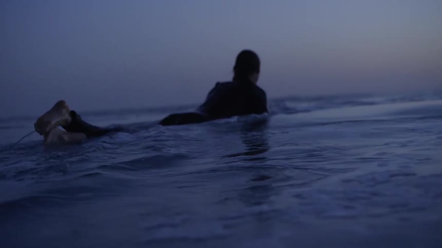Man on a surfboard paddling through the sea on a purple sky morning