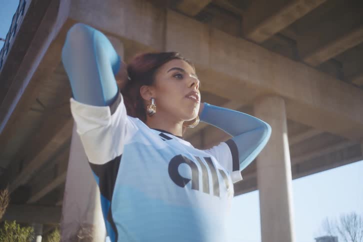 Model below an overpass fixing her hair and posing in a football team shirt