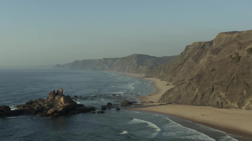 Aerial panorama of a beach with the coast formed by rocky mountain ranges and a cloudless morning sky
