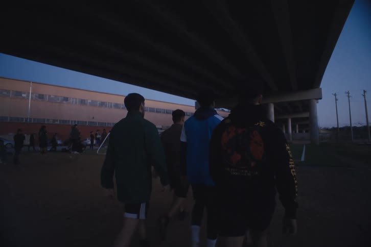 Men approach soccer game played on soccer field under elevated highway
